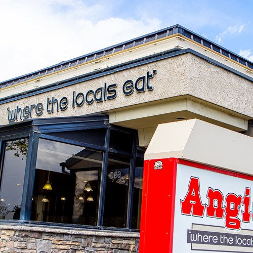 Sign on a restaurant building reads "where the locals eat" with a red sign for "Angie's" in front.