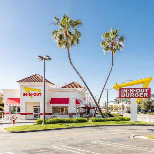 In-N-Out Burger restaurant with palm trees and a clear blue sky in the background.
