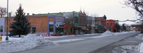 Snow-covered street lined with colorful buildings and festive decorations in a small town during winter.