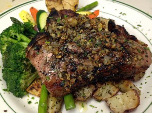 A grilled steak topped with herbs, served on a bed of mixed vegetables and roasted potatoes.