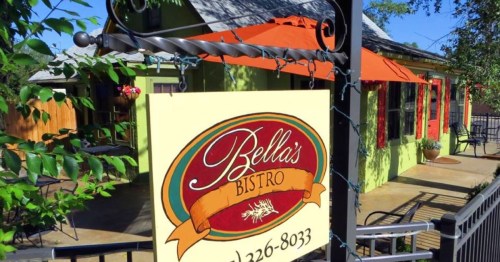 Sign for Bella's Bistro, featuring a colorful design, hanging from a decorative bracket outside a charming building.