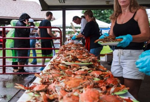 A long table filled with crabs, with people serving and enjoying food at an outdoor event, some wearing gloves.