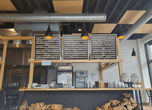 A modern café interior featuring a menu board, coffee station, and stacked firewood in a cozy atmosphere.