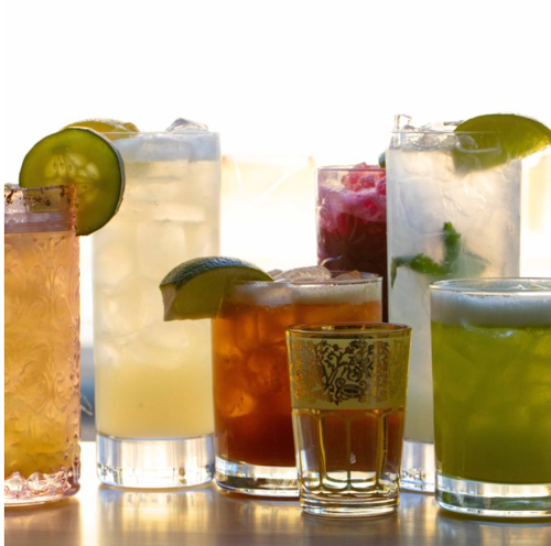 A variety of colorful cocktails in glasses, featuring garnishes like lime and mint, on a wooden table.