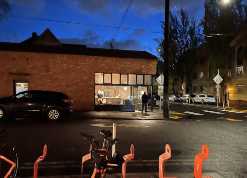 A dimly lit street scene at night, featuring a brick building with large windows and parked cars nearby.