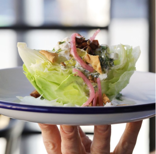 A hand holding a plate with a fresh salad featuring lettuce, toppings, and a creamy dressing.
