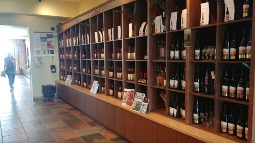 A wooden display shelf filled with various bottles of wine, with a person walking in the background.
