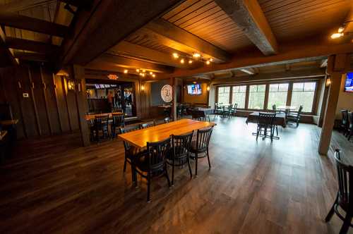 Interior of a rustic restaurant with wooden beams, tables, and large windows overlooking a natural view.