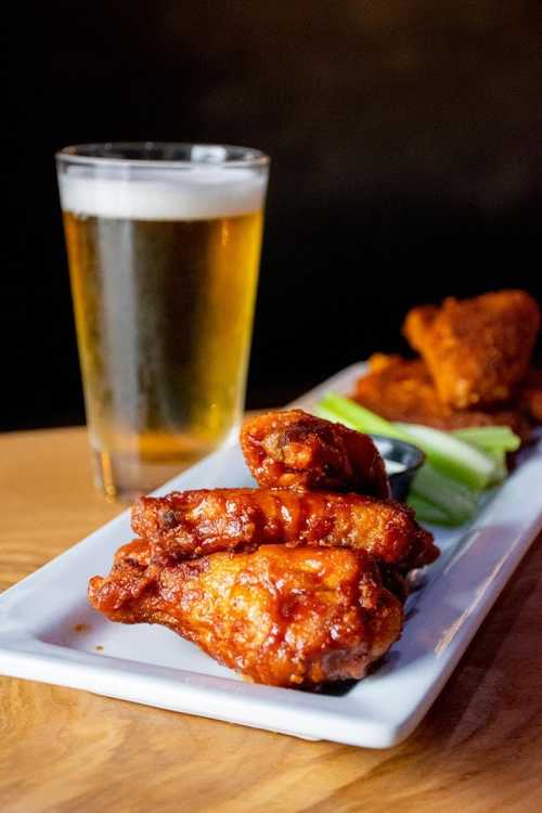 A plate of spicy chicken wings with celery sticks and dipping sauce, alongside a glass of beer.