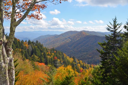 A scenic view of mountains covered in vibrant autumn foliage under a partly cloudy sky.