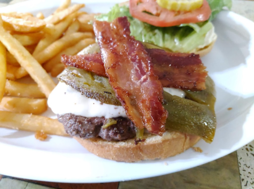 A juicy burger topped with bacon, jalapeños, and mayonnaise, served with crispy fries and a side of lettuce and tomato.