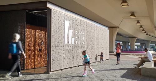 A modern building with a textured facade, people walking by, and children playing nearby under a large overhang.