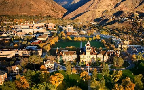 Aerial view of a university campus surrounded by mountains, featuring historic buildings and colorful autumn foliage.