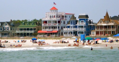 Colorful beach houses line the shore, with people relaxing on the sand and umbrellas dotting the beach.