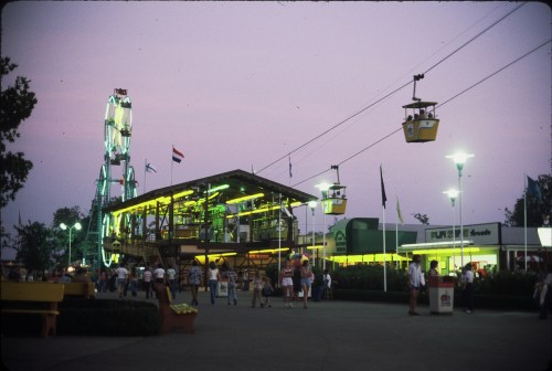 A vibrant amusement park scene at dusk, featuring a ferris wheel, gondola rides, and colorful lights.