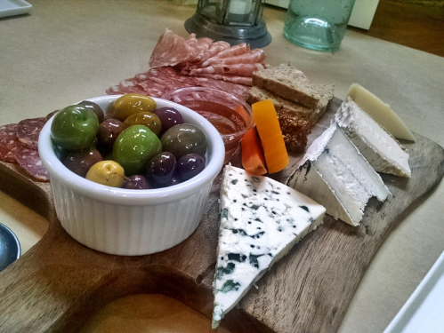 A wooden platter featuring assorted cheeses, cured meats, olives, and bread, arranged artfully for a charcuterie board.