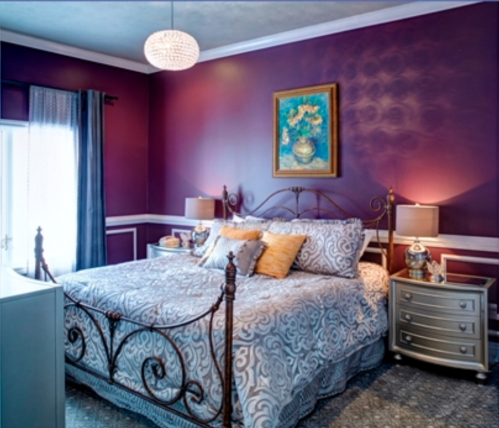 Cozy bedroom with a purple accent wall, ornate bed, decorative pillows, and stylish lamps.