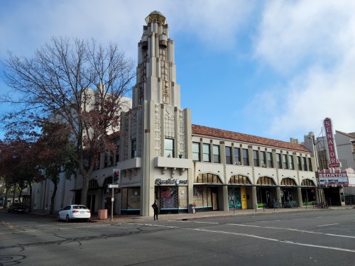 Art Deco building with a tall tower, featuring large windows and a marquee sign reading "Senator." Clear blue sky above.