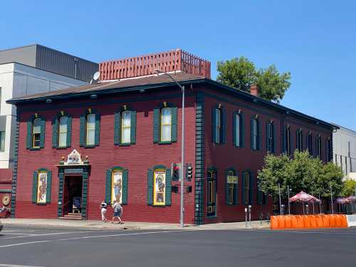 Historic red brick building with green trim, large windows, and decorative murals, located at a street corner.