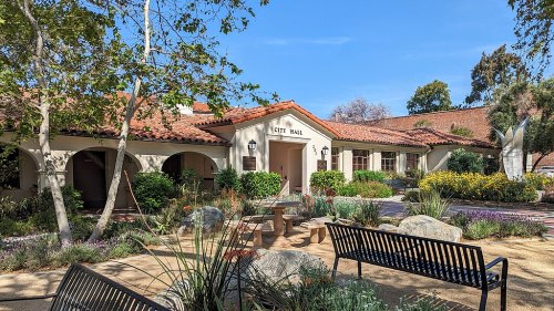 A sunny view of City Hall surrounded by greenery, flowers, and benches, showcasing a welcoming outdoor space.