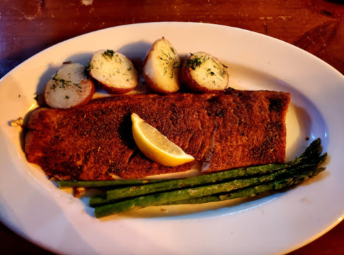 A plate featuring seasoned fish fillet, lemon wedge, roasted potatoes, and asparagus.