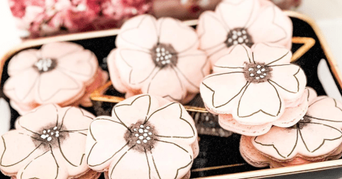 A tray of pink flower-shaped macarons decorated with black outlines and silver embellishments.