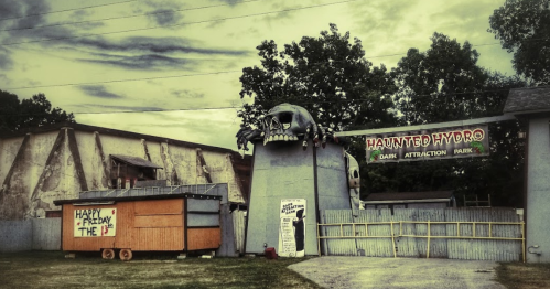 A spooky amusement park entrance featuring a skull and sign for "Haunted Hydro" with a nearby orange trailer.