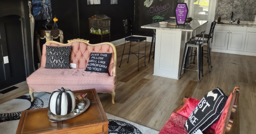 Cozy interior featuring pink and red sofas, a wooden table, and a modern kitchen with bar stools and black walls.