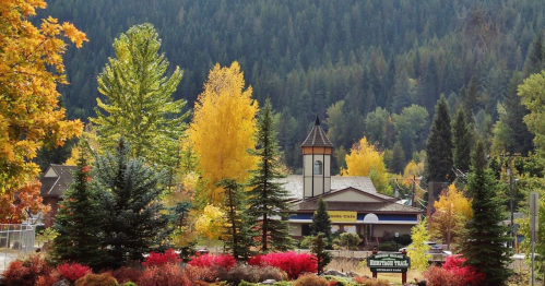 A scenic view of colorful autumn trees surrounding a building, with mountains in the background.
