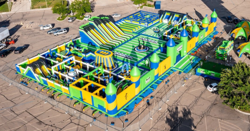 A colorful inflatable playground with slides, obstacles, and towers, set up in a large outdoor area.