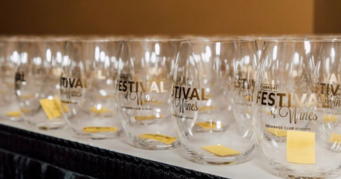A row of clear wine glasses with "Festival of Wines" printed on them, displayed on a table.