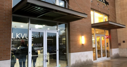 Exterior view of a storefront with glass doors and a sign reading "MILKVUE," featuring a modern design and warm lighting.