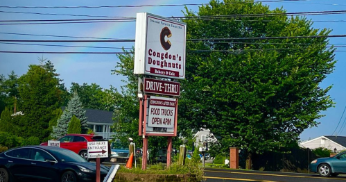 Sign for Congdon's Doughnuts with a drive-thru, food truck info, and a rainbow in the background.