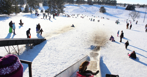 A snowy hill filled with people sledding and enjoying winter activities under a clear blue sky.