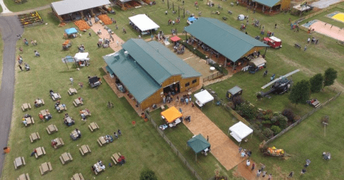 Aerial view of a bustling outdoor event with tents, food stalls, and people enjoying the space on a grassy area.