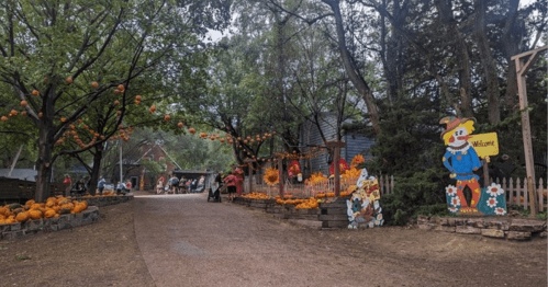 A scenic pathway lined with pumpkins and decorations, leading to a welcoming sign and festive autumn atmosphere.