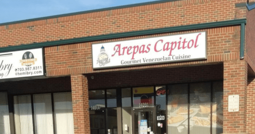 Sign for "Arepas Capitol" featuring gourmet Venezuelan cuisine on a brick storefront.