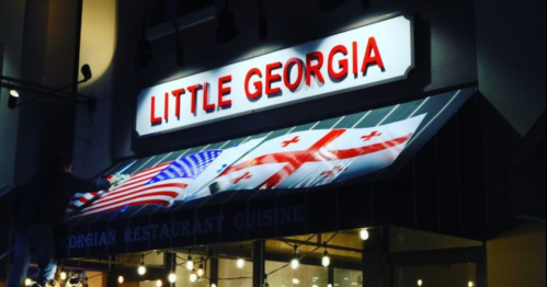 Sign for "Little Georgia" restaurant featuring American and Georgian flags, illuminated at night.