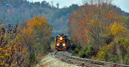 A train travels along a curved track surrounded by colorful autumn foliage.
