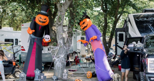Two large inflatable Halloween decorations, a pumpkin in a top hat and a purple figure, surrounded by cobwebs and tombstones.