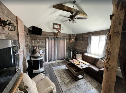 Cozy living room with wooden walls, a sofa, coffee table, and rustic decor, including deer antlers and a ceiling fan.