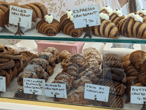 A display of various croissants, including chocolate, almond, and espresso, with price tags in a bakery.