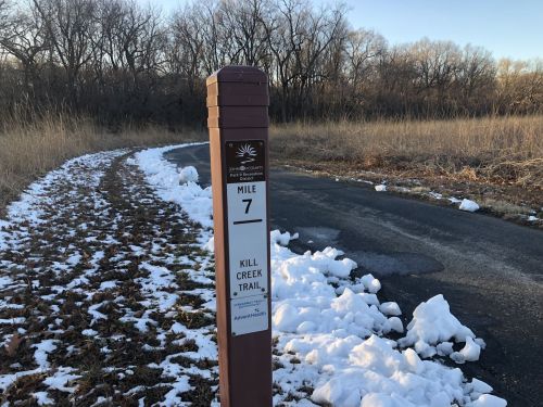 Trail marker indicating Mile 7 on Kill Creek Trail, surrounded by grass and patches of snow.