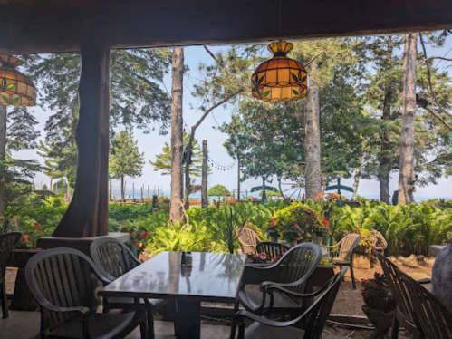 A cozy restaurant patio with a table, surrounded by greenery and trees, overlooking a serene lake view.