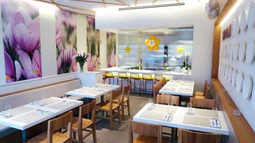 Bright, modern restaurant interior with floral decor, wooden tables, and a bar area in the background.