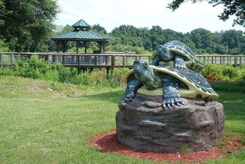 A large turtle sculpture sits on a rock, with a gazebo and lush greenery in the background.