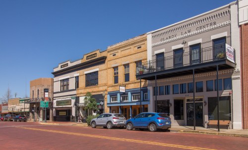 A sunny street view of historic buildings with shops and a law center, featuring parked cars and a clear blue sky.
