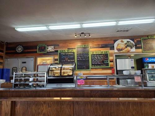 A cozy diner interior with a wooden counter, menu boards, and a display case, featuring daily specials and drinks.