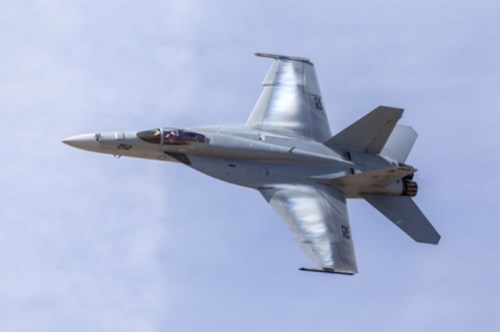 A sleek military jet flying at an angle against a clear blue sky.