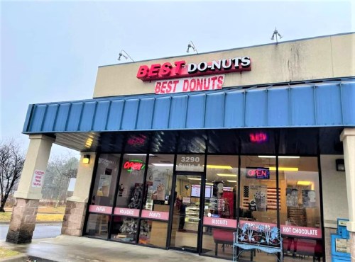 Sign for "Best Do-Nuts" shop with a blue awning, featuring "OPEN" and various food items displayed in the window.